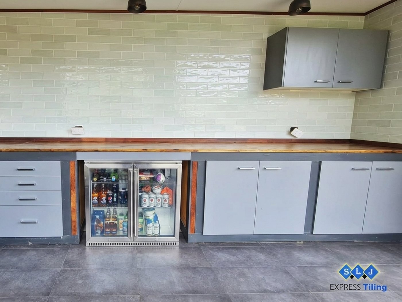 Outdoor kitchen tiled by SLJ Express Tiling & Waterproofing with a green tiled splashback and large-format grey floor tiles