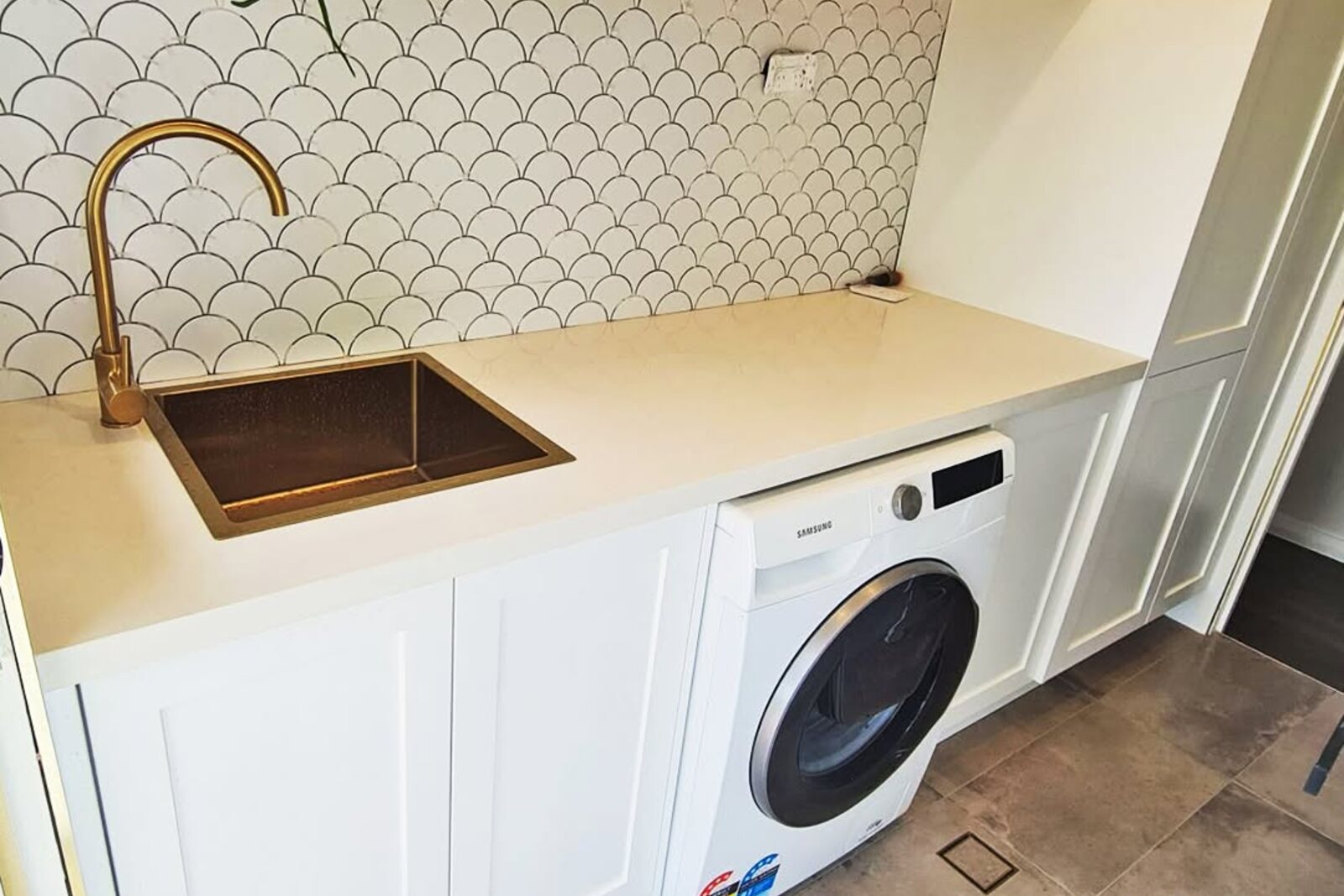 Laundry finished with a gloss white fish-scale splashback, 300x600 ash grey floor tiles and a brass tile-insert drain